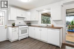 White cabinetry, wood-finish countertops, stainless steel sink, white dishwasher, and wood-finish flooring - 
