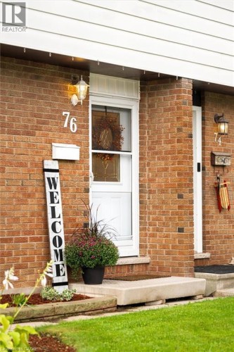 Brick exterior, white siding soffit, front entry door with storm door, wall-mounted light fixtures, concrete porch - 76 Cluthe Crescent, Kitchener, ON 