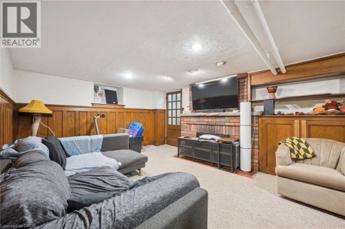 Brick-faced fireplace with a stone mantel, wood paneling, built-in shelving, carpet flooring, and recessed lighting - 143 David Street, Kitchener, ON 