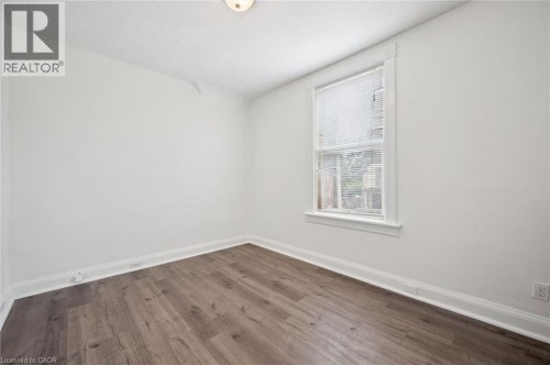 Light-filled room featuring wood-finish flooring, white walls, and a single window with blinds - 143 David Street, Kitchener, ON 