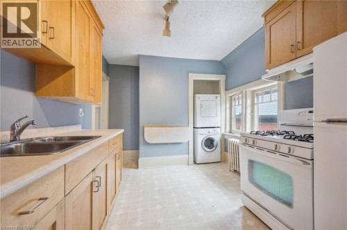 Kitchen featuring light wood cabinetry, dual basin stainless steel sink, white range oven, and a stacked washer and dryer - 143 David Street, Kitchener, ON 