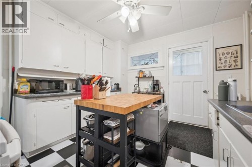 Kitchen featuring white cabinetry, checkered floor tiling, a ceiling fan, and a paneled entry door with an upper window - 143 David Street, Kitchener, ON 