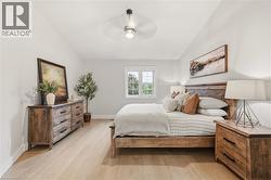Bright bedroom featuring light wood-finish flooring, a ceiling fan with integrated lighting, and a white-framed window - 