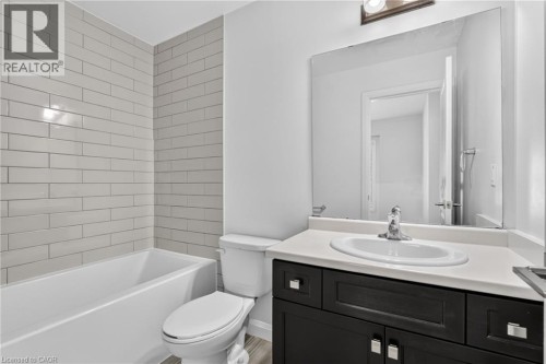 White subway tile surround, built-in bathtub, white toilet, dark wood-finish vanity with a white countertop, and an oval undermount sink - 1169 E Garner Road E Unit# 66, Ancaster, ON 