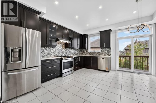 Expansive kitchen featuring dark wood cabinetry, stainless steel appliances, a mosaic tile backsplash, and white tile flooring - 1169 E Garner Road E Unit# 66, Ancaster, ON 
