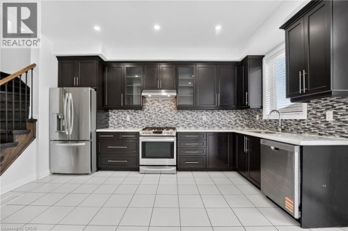 Modern kitchen featuring dark cabinetry with glass-front upper doors, stainless steel appliances including a French-door refrigerator and slide-in range, mosaic tile backsplash, quartz countertops, an - 1169 E Garner Road E Unit# 66, Ancaster, ON 