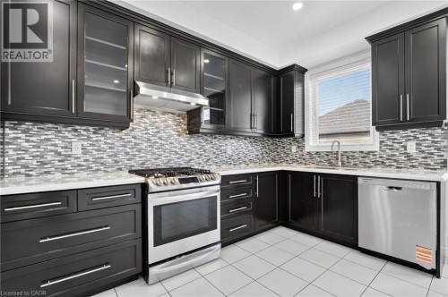 Dark wood cabinetry with glass-front accents, stainless steel appliances, mosaic tile backsplash, white countertops, and tiled flooring - 1169 E Garner Road E Unit# 66, Ancaster, ON 
