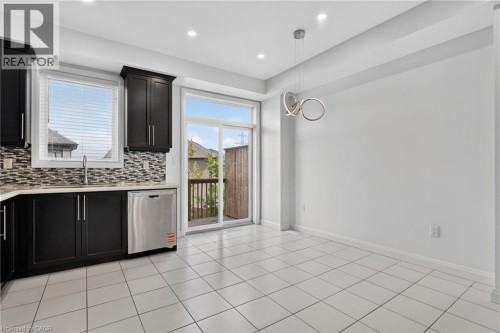 White tile flooring, dark cabinetry, mosaic tile backsplash, stainless steel dishwasher, and a contemporary pendant light fixture - 1169 E Garner Road E Unit# 66, Ancaster, ON 