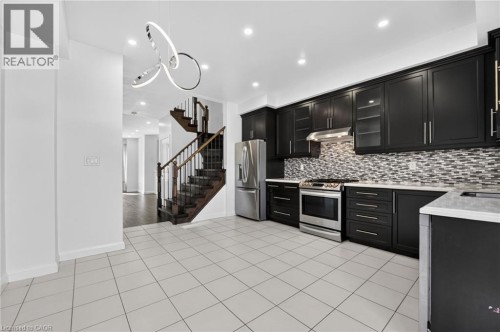 Kitchen featuring dark cabinetry, stainless steel appliances, mosaic tile backsplash, and white tile flooring - 1169 E Garner Road E Unit# 66, Ancaster, ON 
