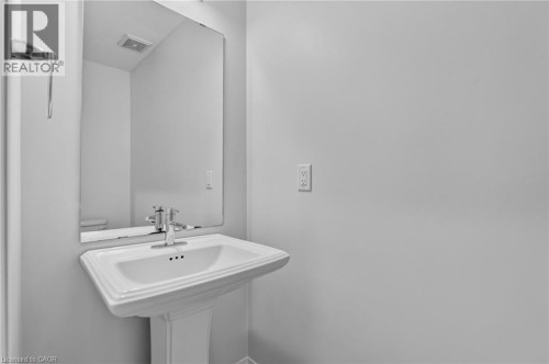 White pedestal sink with chrome faucet, complemented by a rectangular wall-mounted mirror - 1169 E Garner Road E Unit# 66, Ancaster, ON 