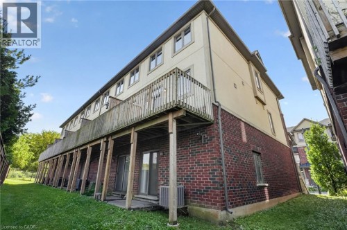 Exterior featuring a wood deck, brick first story, light-colored upper story, multiple windows, and a grass lawn - 1169 E Garner Road E Unit# 66, Ancaster, ON 