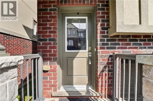 Welcoming brick entrance featuring a sage-green paneled door with glass inset, flanked by black metal railings and stone-capped pillars - 1169 E Garner Road E Unit# 66, Ancaster, ON 