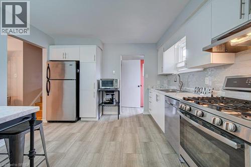 Kitchen featuring wood-finish flooring, white cabinetry, stainless steel appliances, and a tiled backsplash - 3158 Palmer Drive, Burlington, ON 