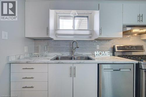White cabinetry and drawers with stainless steel pulls, dual basin stainless steel sink, stainless steel faucet, patterned countertop, and light-toned backsplash - 3158 Palmer Drive, Burlington, ON 