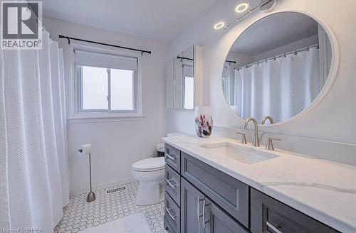 Bathroom featuring a dual-sink vanity with a light-toned countertop, gray shaker-style cabinetry, and a circular mirror - 3158 Palmer Drive, Burlington, ON 