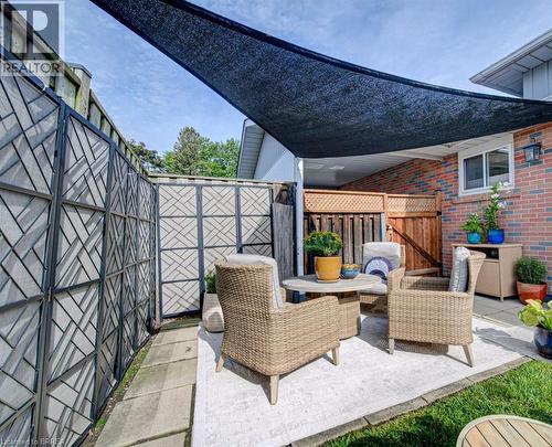 Patio space featuring a black shade sail, brick exterior, lattice-top wooden fencing, and decorative privacy screens - 3158 Palmer Drive, Burlington, ON 