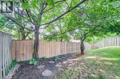 Expansive backyard featuring mature trees, a wooden privacy fence, a stepping stone path, and an inclined grassy area - 3158 Palmer Drive, Burlington, ON 