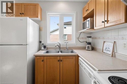 Kitchen featuring wood-finish cabinetry, a double basin stainless steel sink, laminate countertops, and a white tile backsplash - 67 Apple Tree Drive, Kitchener, ON 