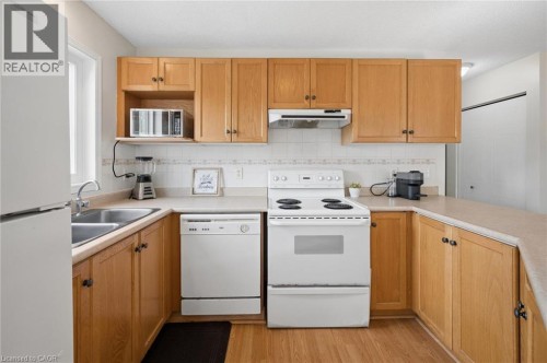 Kitchen featuring wood-finish cabinetry, a double basin stainless steel sink, tile backsplash, and light-toned countertops - 67 Apple Tree Drive, Kitchener, ON 