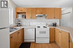 Kitchen featuring wood-finish cabinetry, a double basin stainless steel sink, tile backsplash, and light-toned countertops - 