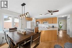 Open-concept living space featuring wood-finish flooring, a kitchen with light wood cabinetry, a breakfast bar, and white appliances - 