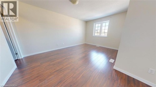 Spacious room with wood-finish flooring, neutral wall tones, and a multi-pane window - 11 Sorrento Street, Kitchener, ON 