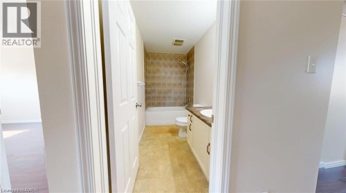 Bathroom featuring a white vanity with dual sinks, a white toilet, a white bathtub with a tiled shower surround, and light-toned flooring - 11 Sorrento Street, Kitchener, ON 