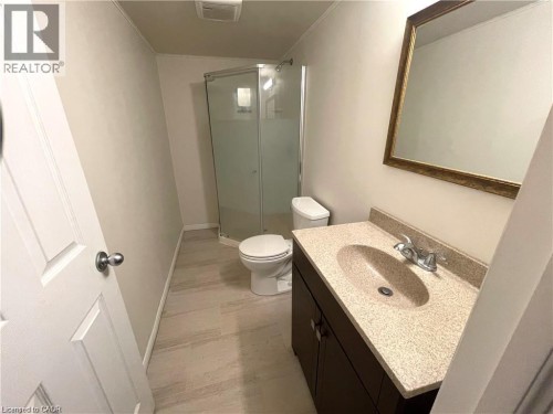 Bathroom featuring a corner shower with glass enclosure, single vanity with integrated sink, dark wood-finish cabinetry, and neutral-toned flooring - 11 Sorrento Street, Kitchener, ON 