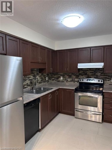 Kitchen featuring wood-finish cabinetry, stainless steel appliances, mosaic tile backsplash, double basin sink, and light-toned flooring - 11 Sorrento Street, Kitchener, ON 