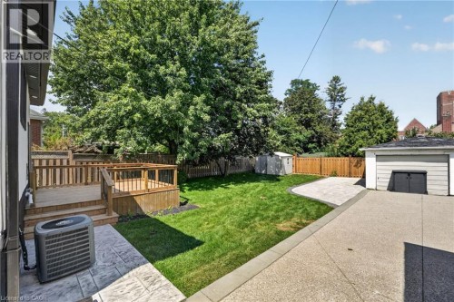 Expansive backyard featuring a multi-level wood deck, manicured lawn, concrete patio, and detached garage - 43 Brucedale Avenue E, Hamilton, ON 