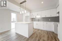 Kitchen featuring white cabinetry, gray subway tile backsplash, white countertop island, wood-finish flooring, and recessed lighting - 