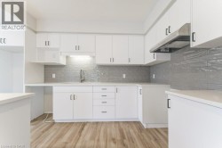 White cabinetry with matte black hardware, light-toned countertops, grey subway tile backsplash, wood-finish flooring, and stainless steel range hood - 