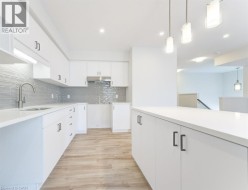 Modern kitchen featuring white cabinetry, light-toned countertops, a full-height gray subway tile backsplash, stainless steel range hood, and wood-finish flooring - 