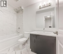 White marbled tile flooring, white marbled tile shower surround, white bathtub, dark wood-finish vanity, and a light fixture with three sconces - 