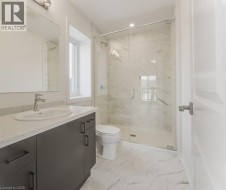 Bathroom featuring a glass-enclosed shower, dark wood-finish vanity with an integrated sink, light speckled countertop, and white patterned floor tiles - 