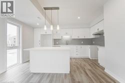 Kitchen featuring an island, white cabinetry, a gray tiled backsplash, wood-finish flooring, and a large window - 