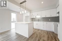 Kitchen featuring white cabinetry, gray subway tile backsplash, white countertop island, wood-finish flooring, and recessed lighting - 
