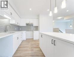 Modern kitchen featuring white cabinetry, light-toned countertops, a full-height gray subway tile backsplash, stainless steel range hood, and wood-finish flooring - 