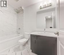 White marbled tile flooring, white marbled tile shower surround, white bathtub, dark wood-finish vanity, and a light fixture with three sconces - 