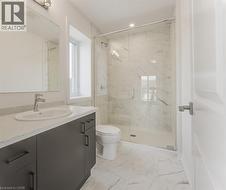 Bathroom featuring a glass-enclosed shower, dark wood-finish vanity with an integrated sink, light speckled countertop, and white patterned floor tiles - 