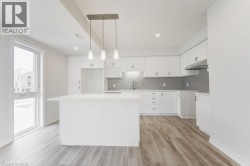 Kitchen featuring an island, white cabinetry, a gray tiled backsplash, wood-finish flooring, and a large window - 