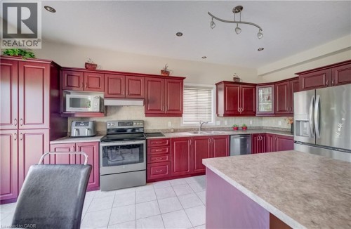 L-shaped kitchen featuring wood-finish cabinetry, stainless steel appliances, and a central island with a contrasting base - 573 Robert Ferrie Drive, Kitchener, ON 