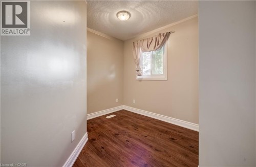 Wood-finish flooring, single window, white trim, crown molding, and a flush-mount ceiling light - 573 Robert Ferrie Drive, Kitchener, ON 