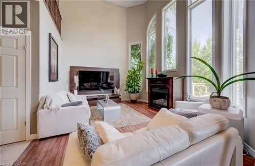 Two-story living area with high ceilings, wood-finish flooring, a built-in electric fireplace, and expansive windows - 573 Robert Ferrie Drive, Kitchener, ON 