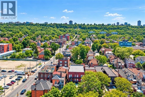 Aerial perspective featuring a residential area with varied architectural styles, tree-lined streets, and distant city structures - 663 King Street E, Hamilton, ON 