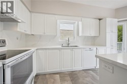 White shaker-style cabinetry with chrome hardware, full-height quartz backsplash, stainless steel sink with gooseneck faucet, integrated dishwasher, and wood-finish flooring - 