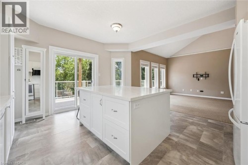 Kitchen island with a light-toned countertop, sliding glass door access to an exterior deck, vaulted ceilings, and a series of three windows - 426 Hidden Creek Drive, Kitchener, ON 
