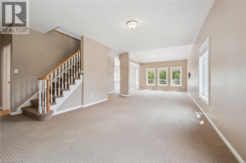 Spacious interior with neutral carpeting, a wood and white spindle staircase, multiple large windows, and a vaulted ceiling - 426 Hidden Creek Drive, Kitchener, ON 