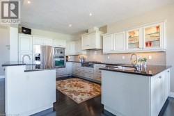 Gourmet kitchen featuring white cabinetry with glass-front upper cabinets, stainless steel appliances, black granite countertops, subway tile backsplash, and a dual-island layout with ample counter sp - 