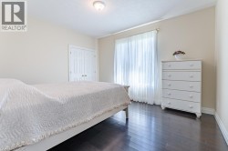 Spacious primary bedroom with dark wood-finish flooring, white bi-fold closet doors, and abundant natural light from sliding glass doors with sheer curtains - 